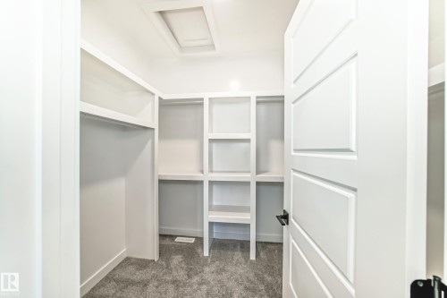 Walk-in closet featuring white built-in shelving, hanging rods, and gray carpet flooring - 341 Roberts Wynd, Leduc, AB 