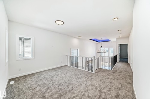 Carpeted upper-level landing featuring a metal spindle railing system, multiple windows, recessed lighting, and a chandelier with a blue-lit ceiling detail - 341 Roberts Wynd, Leduc, AB 