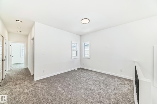 Neutral toned carpeted area featuring two windows with horizontal blinds, white baseboards, and a contemporary ceiling light fixture - 341 Roberts Wynd, Leduc, AB 
