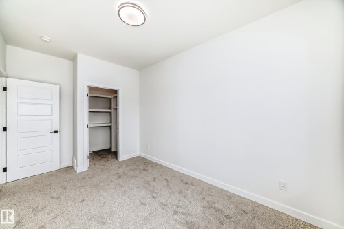 Neutral toned carpeting complementing white walls, a flush-mount ceiling light, a built-in closet with shelving and hanging rod, and a five-panel interior door with matte black hardware - 341 Roberts Wynd, Leduc, AB 