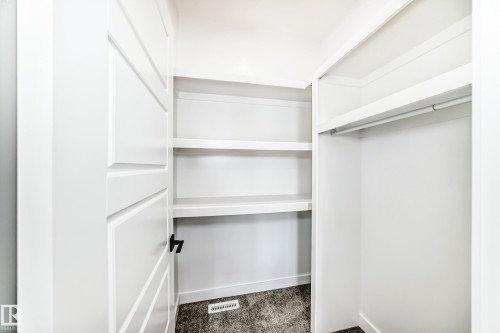 Recessed closet featuring white built-in shelving, a clothes rod, and dark carpet flooring - 341 Roberts Wynd, Leduc, AB 