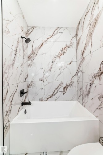 Bathroom featuring a white soaking tub with matte black fixtures, surrounded by large format porcelain wall tiles with a prominent veining pattern - 341 Roberts Wynd, Leduc, AB 