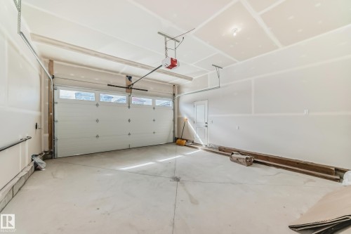 Spacious garage featuring a concrete floor, an overhead garage door with upper window panels, and an interior access door - 341 Roberts Wynd, Leduc, AB 