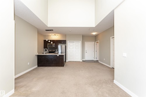 Open-concept living space featuring a kitchen with dark wood cabinetry, stainless steel appliances, a breakfast bar, and pendant lighting - 505 1230 Windermere Way, Edmonton, AB 
