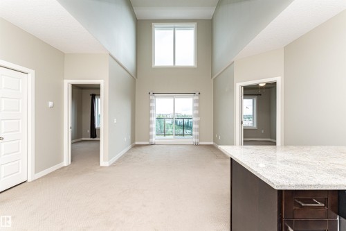 Spacious living area featuring high ceilings, light beige wall paint, and beige carpet flooring - 505 1230 Windermere Way, Edmonton, AB 