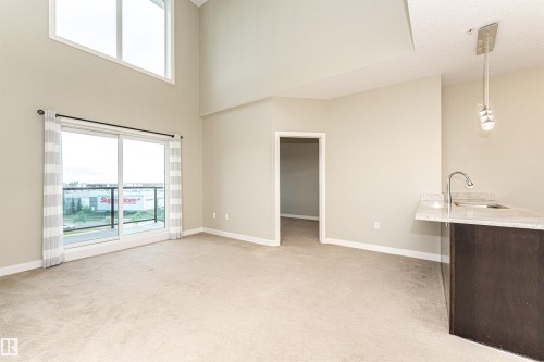 Living area featuring high ceilings, a sliding glass door to a balcony, an upper transom window, and carpet flooring - 505 1230 Windermere Way, Edmonton, AB 