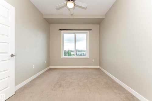 Neutral-toned interior with light-colored carpet flooring, white baseboards, and a window featuring a dark curtain rod - 505 1230 Windermere Way, Edmonton, AB 