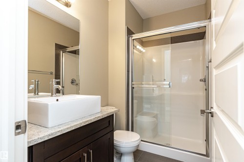 Bathroom featuring a dark wood-finish vanity with a light speckled countertop, a rectangular vessel sink, and a glass-enclosed shower with sliding doors - 505 1230 Windermere Way, Edmonton, AB 