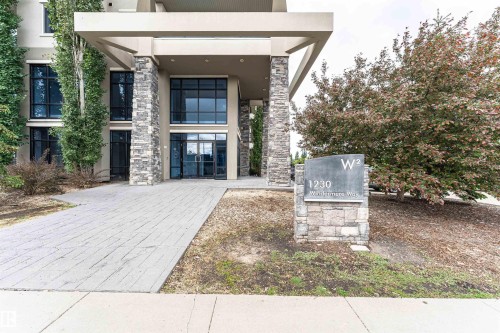 Contemporary building entrance featuring stone veneer columns, expansive windows, and a paved walkway - 505 1230 Windermere Way, Edmonton, AB 