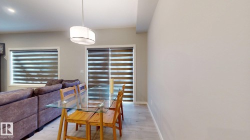 Open-concept living space featuring light wood-finish flooring, a contemporary drum pendant light, and a patio door with horizontal blinds - 607 31 Avenue, Edmonton, AB 
