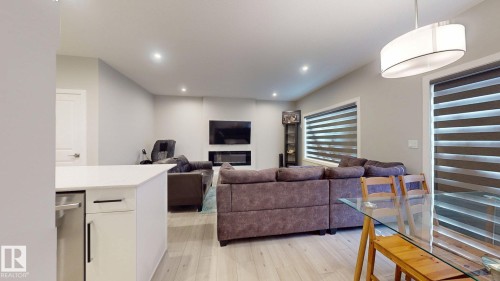 Open-concept living area featuring light wood-finish flooring, recessed lighting, and a contemporary fireplace with a built-in television mount - 607 31 Avenue, Edmonton, AB 