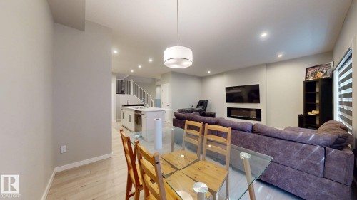 Open-concept living space with wood-finish flooring, recessed ceiling lighting, a built-in electric fireplace, a kitchen island, and a staircase with white balusters - 607 31 Avenue, Edmonton, AB 