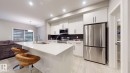 Modern kitchen featuring an island with a built-in sink, white cabinetry, integrated stainless steel appliances, a dark tile backsplash, and recessed lighting - 607 31 Avenue, Edmonton, AB 
