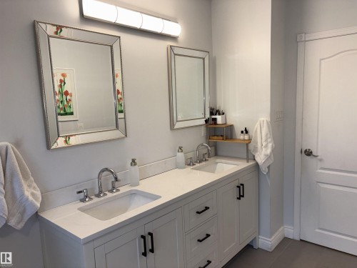 Bathroom featuring a double vanity with light-colored countertops, dual undermount sinks, chrome fixtures, and white shaker-style cabinetry with black pulls - 14016 85 Avenue, Edmonton, AB 