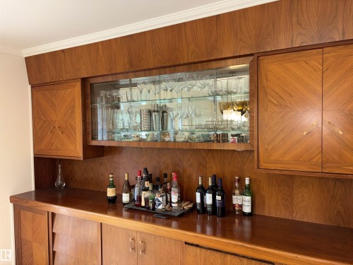 Custom built-in cabinetry featuring wood-finish construction with a patterned inlay, glass-front display shelving, an integrated counter surface, and matching base storage - 14016 85 Avenue, Edmonton, AB 