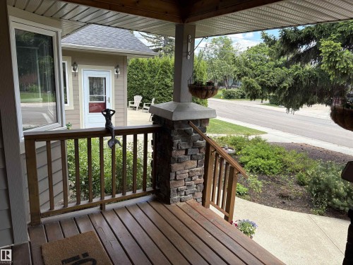 Inviting covered front porch with wood-finish decking, stone-clad pillar, and wood railing - 14016 85 Avenue, Edmonton, AB 