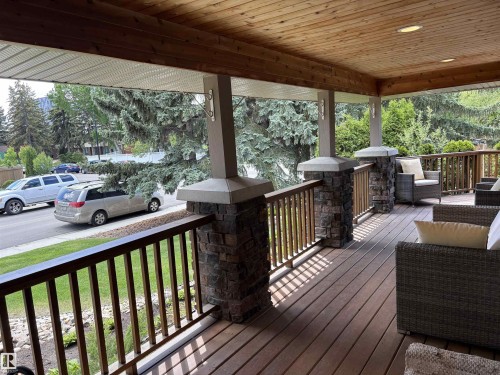Spacious covered porch featuring a wood-finish plank deck, stone-accented columns, wood-paneled ceiling, and recessed lighting - 14016 85 Avenue, Edmonton, AB 