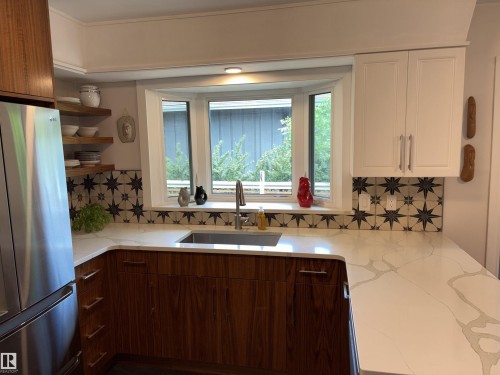 Kitchen featuring a bay window, white countertops with veining, wood-finish lower cabinetry, white upper cabinetry, and patterned tile backsplash - 14016 85 Avenue, Edmonton, AB 