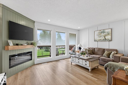 Living area featuring wood-finish flooring, a corner fireplace with a wood mantle, and an integrated media wall - 9 Millgrove Drive, Spruce Grove, AB 