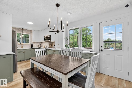 Kitchen and dining area featuring a modern black chandelier, wood-finish flooring, white upper cabinetry, and contrasting green lower cabinetry - 9 Millgrove Drive, Spruce Grove, AB 