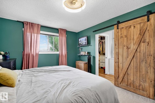 Bedroom featuring a wood barn door, built-in shelving, and a window with a white frame - 9 Millgrove Drive, Spruce Grove, AB 