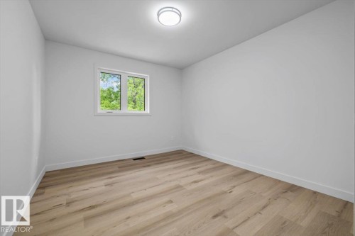 Bright interior space featuring light wood-finish flooring, white baseboards, and a contemporary flush-mount ceiling light - 7 Glacier Place, St. Albert, AB 