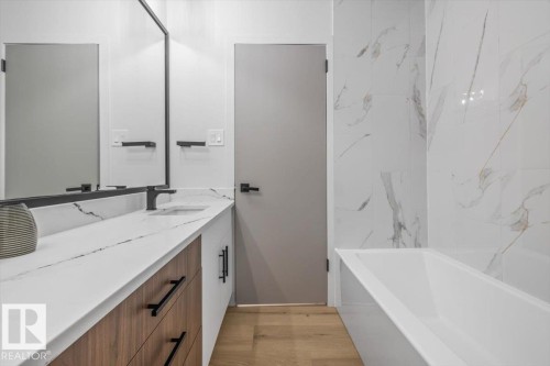 Contemporary bathroom featuring a long wood-finish vanity with matte black hardware, a white countertop with grey veining, a rectangular undermount sink with a matte black faucet, and a large black-framed mirror - 7 Glacier Place, St. Albert, AB 