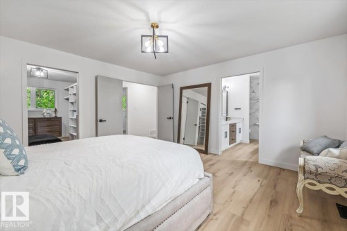 Spacious room featuring wood-finish flooring, a modern ceiling light fixture, a walk-in closet with built-in shelving, and an en-suite bathroom with a vanity and tiled shower - 7 Glacier Place, St. Albert, AB 