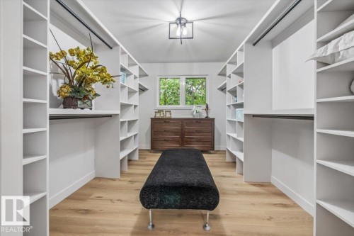 Walk-in closet featuring extensive built-in shelving, hanging rods, light wood-finish flooring, and a ceiling-mounted light fixture - 7 Glacier Place, St. Albert, AB 