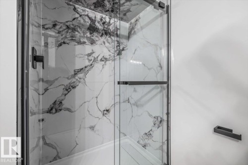 Glass-enclosed shower featuring large format marble-look wall tiling, a black-framed door, and matte black fixtures - 7 Glacier Place, St. Albert, AB 