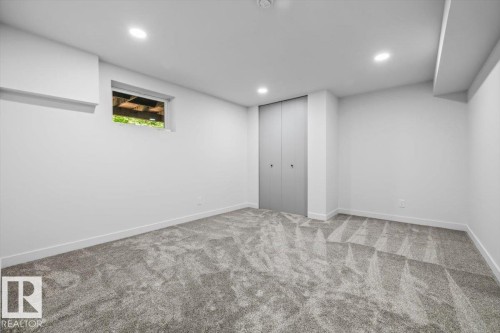 Spacious room featuring neutral grey patterned carpeting, crisp white walls, recessed ceiling lighting, a window with exterior visibility, and a bi-fold closet - 7 Glacier Place, St. Albert, AB 