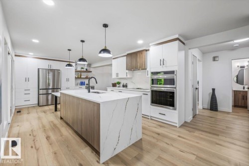 Kitchen featuring a waterfall island with stone countertop, wood-finish flooring, stainless steel appliances, built-in double ovens, and recessed lighting - 7 Glacier Place, St. Albert, AB 