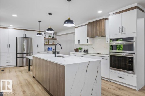 Spacious kitchen featuring an expansive island with a waterfall countertop, integrated sink, and modern pendant lighting - 7 Glacier Place, St. Albert, AB 