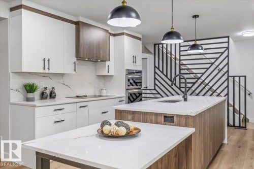 Contemporary kitchen featuring white cabinetry with dark wood accents, integrated stainless steel appliances, a white stone backsplash, and wood-finish flooring - 7 Glacier Place, St. Albert, AB 