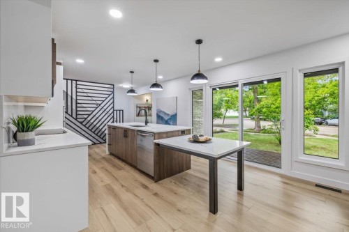 Open-concept kitchen featuring an island with integrated stainless steel appliances, pendant lighting, and wood-finish flooring - 7 Glacier Place, St. Albert, AB 