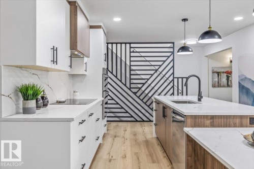Modern kitchen featuring white cabinetry, wood-finish island with integrated sink, sleek black faucet, and white countertops with matching backsplash - 7 Glacier Place, St. Albert, AB 