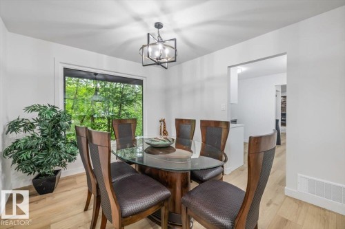 Dining space featuring wood-finish flooring, a contemporary chandelier, and a large window overlooking lush greenery - 7 Glacier Place, St. Albert, AB 