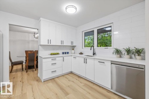 Modern kitchen featuring white cabinetry, light-toned wood-finish flooring, a stainless steel dishwasher, a black matte faucet, and a large window - 7 Glacier Place, St. Albert, AB 