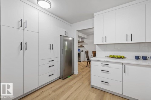 featuring extensive white cabinetry, stainless steel freezer, white subway tile backsplash, light wood-finish flooring, and white countertops - 7 Glacier Place, St. Albert, AB 
