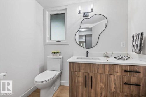Bathroom featuring a wood-finish vanity with a white countertop and integrated sink, a modern black-framed mirror, and a contemporary wall-mounted light fixture - 7 Glacier Place, St. Albert, AB 