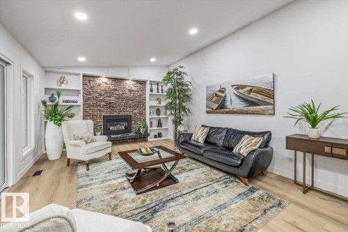 Living area featuring a brick-accented fireplace with a black hearth, built-in shelving, recessed lighting, and light wood-finish flooring - 7 Glacier Place, St. Albert, AB 