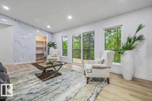 Spacious interior featuring a marble-patterned accent wall, recessed lighting, wood-finish flooring, and a sliding glass door leading to an outdoor deck - 7 Glacier Place, St. Albert, AB 