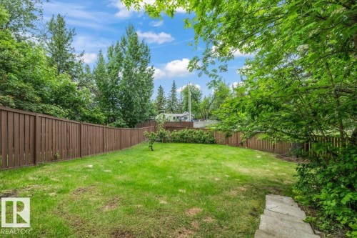 Expansive backyard featuring a lush green lawn, full perimeter wood fencing, mature trees, and concrete stepping stones - 7 Glacier Place, St. Albert, AB 