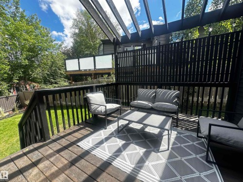 Wood deck featuring a black slatted privacy screen, overhead pergola, black railings, and a grass lawn - 38 Woodcrest Avenue, St. Albert, AB 