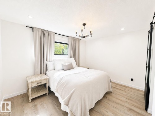 Bright room featuring wood-finish flooring, a contemporary chandelier, recessed ceiling lighting, a window with dark framing, and a dark-framed barn door - 38 Woodcrest Avenue, St. Albert, AB 