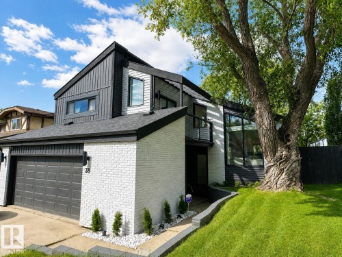 Modern exterior featuring white painted brick, dark vertical siding, a two-car garage, and a sloped lawn with mature tree - 38 Woodcrest Avenue, St. Albert, AB 