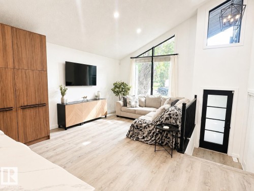 Vaulted ceilings define this living space featuring abundant natural light, wood-finish flooring, and a modern black-framed window - 38 Woodcrest Avenue, St. Albert, AB 