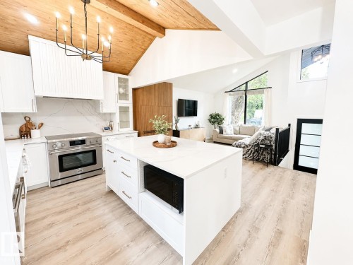 Open-concept kitchen featuring white cabinetry, a large central island with quartz countertop, stainless steel range, and wood-finish flooring - 38 Woodcrest Avenue, St. Albert, AB 