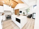 Open-concept kitchen featuring white cabinetry, a large central island with quartz countertop, stainless steel range, and wood-finish flooring - 38 Woodcrest Avenue, St. Albert, AB 