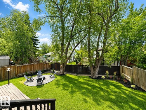 Expansive backyard featuring a manicured lawn, a wood deck, and a stone-paved fire pit area - 38 Woodcrest Avenue, St. Albert, AB 
